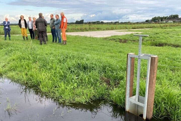 Foto van hand met kluit aarde en in de achtergrond een wegrijdende trekker op een weiland