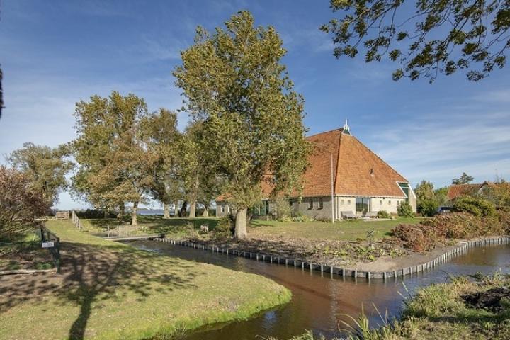 Foto van woonboerderij omringd door sloten en hoge bomen