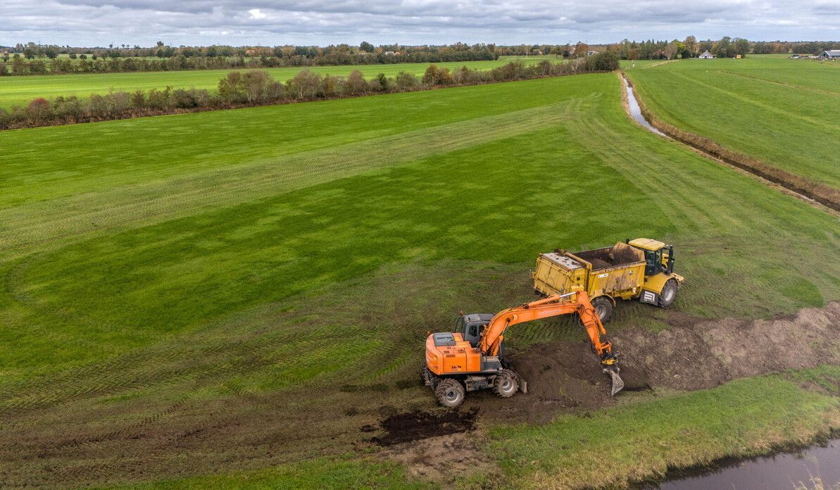 Een luchtfoto van een weiland met op de voorgrond een kraan en een meststrooier