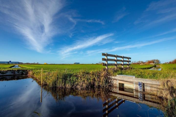 Foto van hek in weiland naast sloot met peilaanduiding