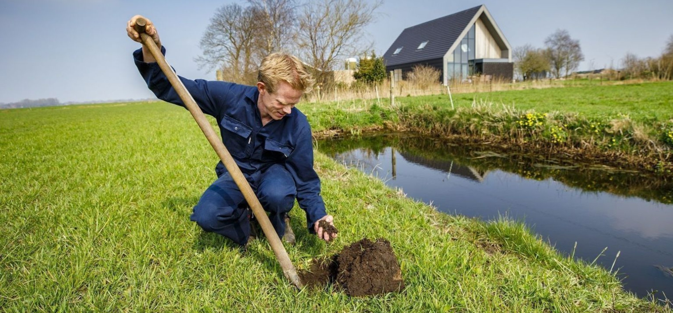 Foto van man in overall die met een spade een kluit grond opschept en opraapt