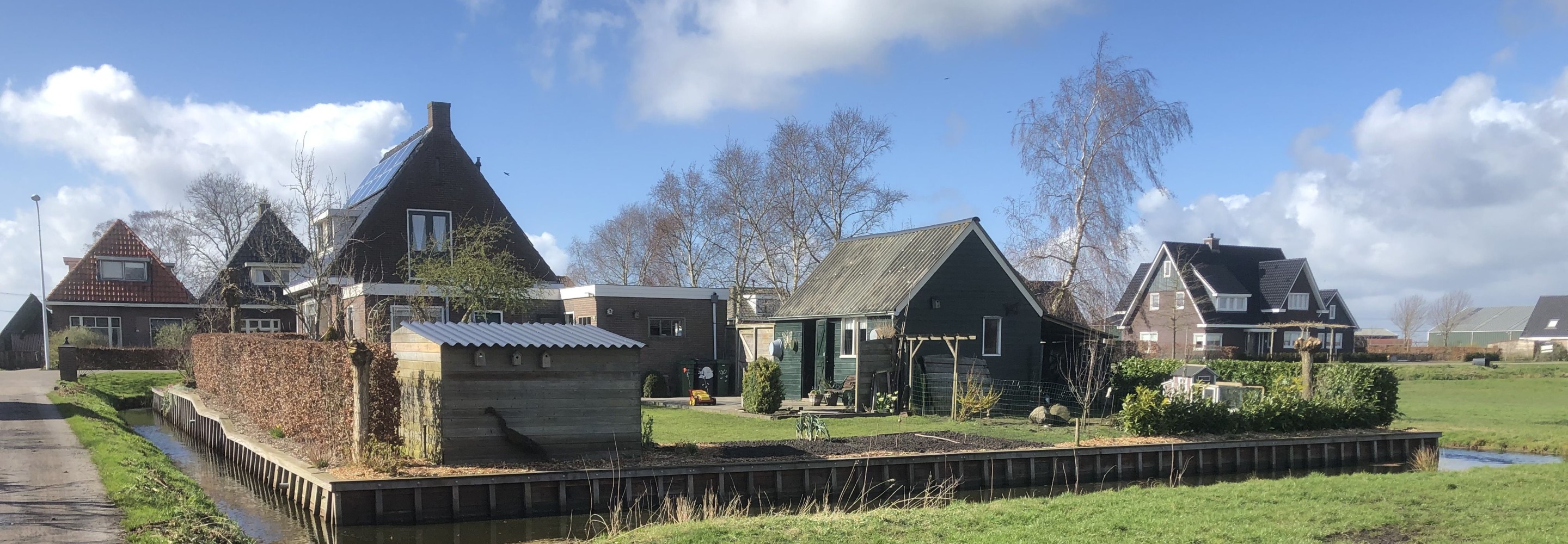 Foto van een rij huizen met erachter een hoogwatercircuit en gras op de voorgrond