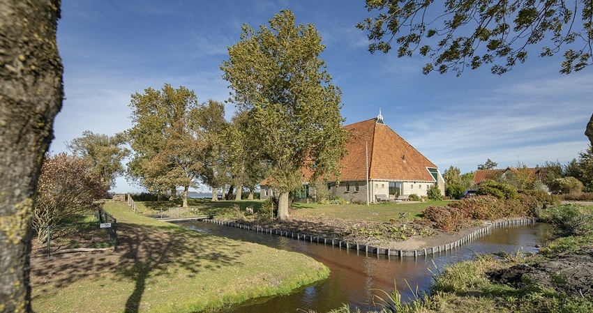 Foto van woonboerderij omringd door sloten en hoge bomen